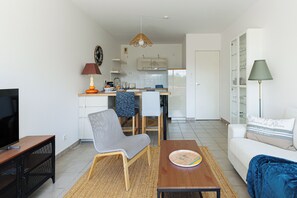 A compact living space with a kitchenette, a dining area, a sofa, and a television. - The Balcony of the Port in Capbreton - Welkeys (Capbreton)