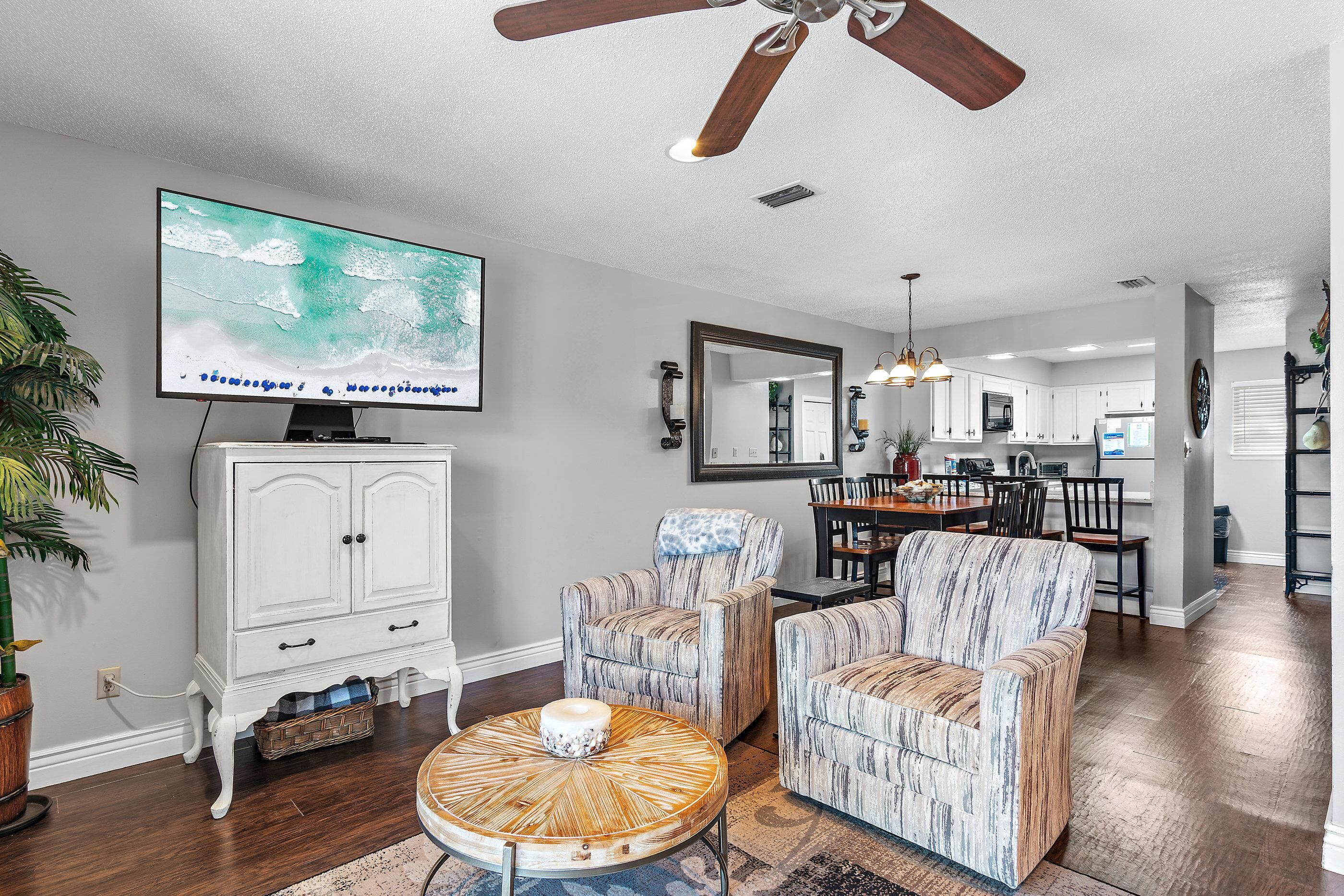A living room with a television, white cabinet, striped armchairs, and a dining area with a table and chairs.