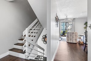 Eine Treppe mit weißen Geländern und dunklen Holzstufen, ein Deckenventilator und ein Blick auf einen Balkon mit Gartenmöbeln.