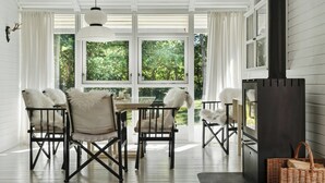 Uma sala de jantar com mesa e cadeiras, lareira e janelas amplas com vista para o verde.