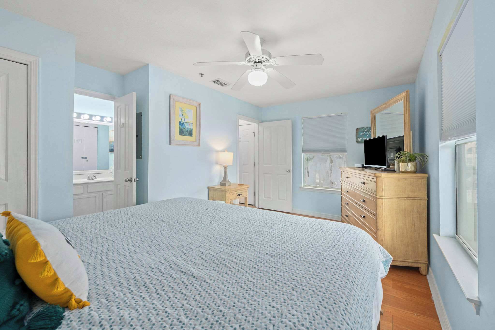 A bedroom with a bed, a ceiling fan, a dresser, a TV, and a window.
