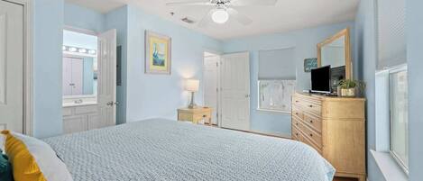 A bedroom with a bed, a ceiling fan, a dresser, a TV, and a window.