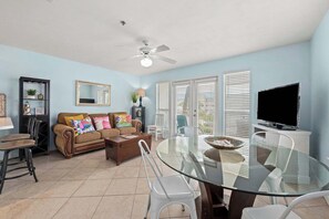 A living room with a glass dining table, a sofa with colorful cushions, a ceiling fan, and a TV. - My SonShine-Hot Tub & Heated Pool-BeachView (Destin)