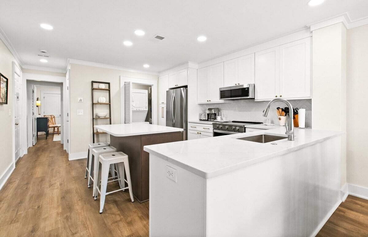 A modern kitchen with white cabinetry, stainless steel appliances, and a central island with stools.