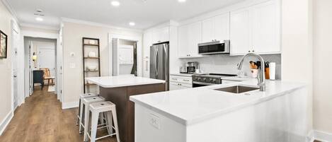 A modern kitchen with white cabinetry, stainless steel appliances, and a central island with stools.
