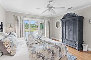 Ein Schlafzimmer mit Bett, Vorhängen, Deckenventilator, Kleiderschrank und Blick durch eine Glastür.