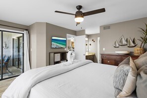 Une chambre d’hôtel avec un lit, un ventilateur de plafond, une télévision, un bureau, une commode et une vue sur l’extérieur, visible à travers une porte vitrée.