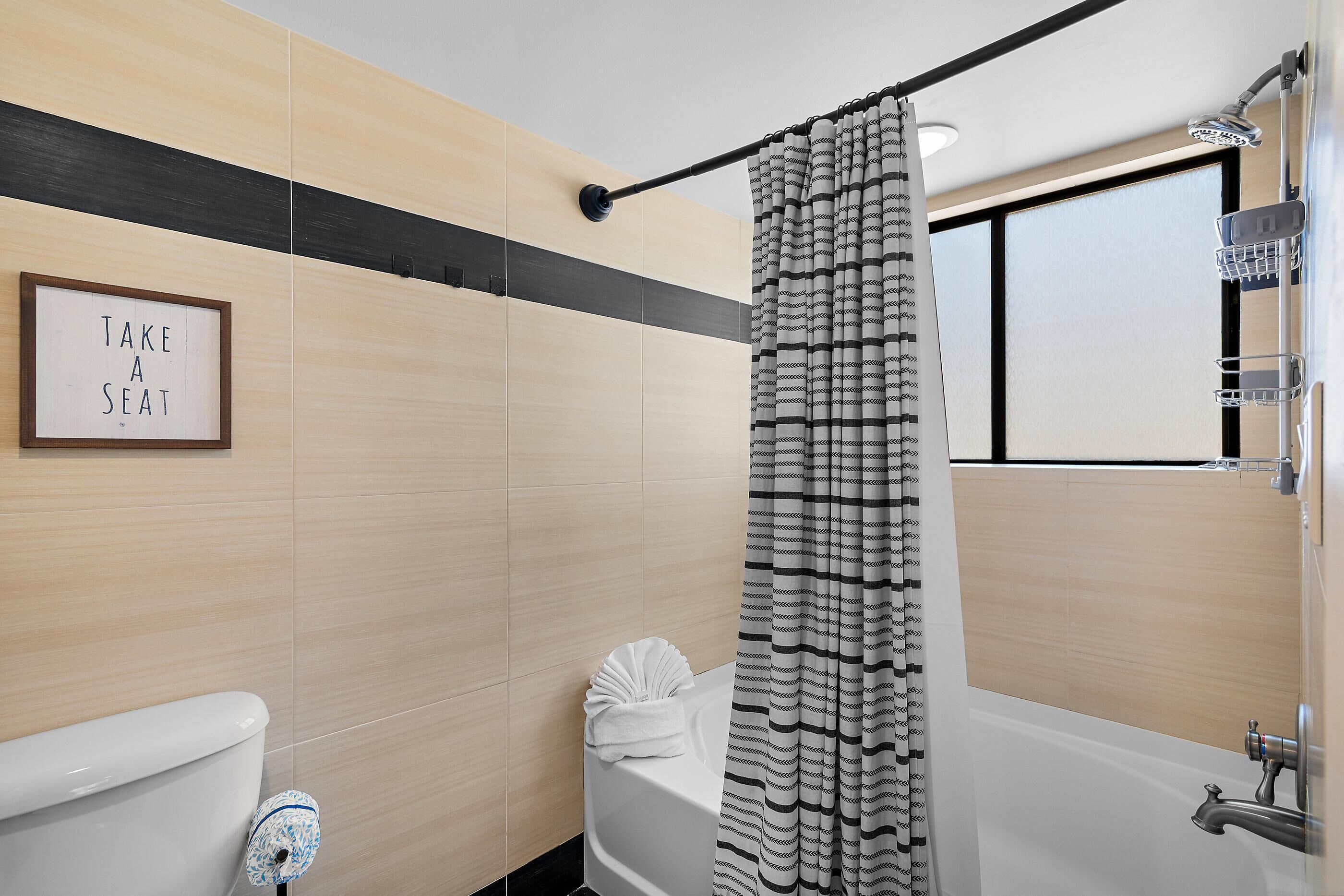 Une salle de bain moderne équipée de toilettes, d’une baignoire, d’une douche et d’un panneau indiquant « PRIEZ DE VOUS ASSEOIR ».