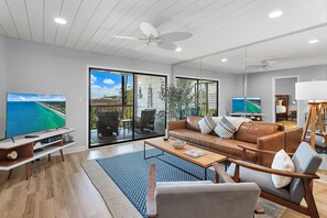 A modern living room with a sofa, coffee table, TV, and a balcony with a view. - Heron's Haven (Miramar Beach)