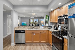 A modern kitchen with granite countertops, stainless steel appliances, wooden cabinets, and a dishwasher. - Heron's Haven (Miramar Beach)