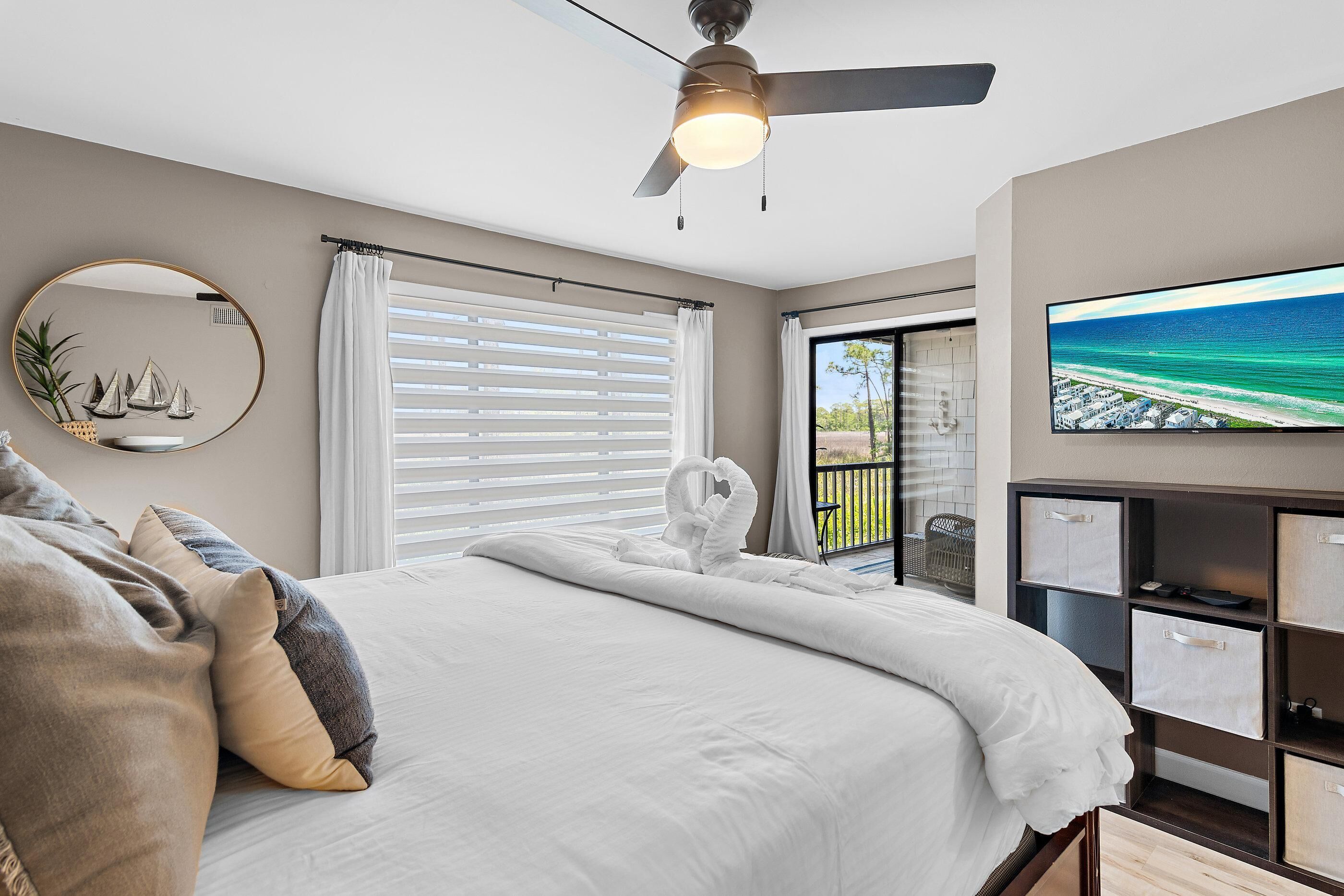 A bedroom with a bed, a ceiling fan, a TV, and a view of the ocean.