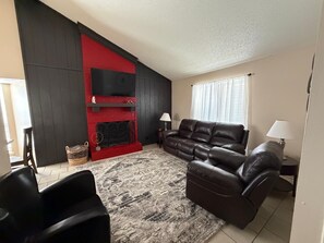 Una sala de estar con chimenea roja, sofá de cuero y alfombra estampada.