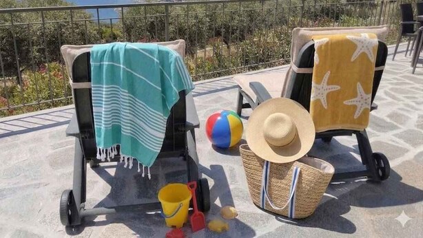 Una terrazza con due sdraio, un pallone da spiaggia, un cappello di paglia e una borsa da mare.