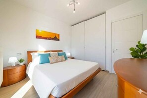Ein Schlafzimmer mit Bett, Nachttisch, Lampe, Pflanze, Kleiderschrank und einem Bild an der Wand.