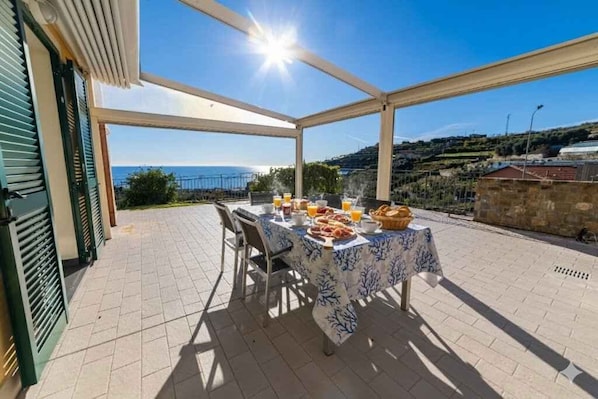 Un'area pranzo all'aperto coperta, con tavolo apparecchiato per la colazione, affacciata su un paesaggio pittoresco.