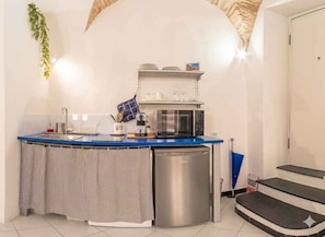 Eine kleine Küche mit blauer Arbeitsplatte, einer Mikrowelle, einer Kaffeemaschine und einem kleinen Kühlschrank.