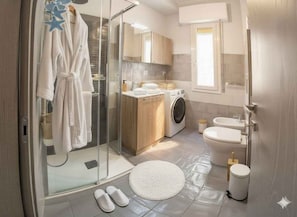 Ein modernes Badezimmer mit Glasdusche, Waschmaschine, Toilette und Waschbecken.