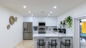 A modern kitchen with white cabinetry, stainless steel appliances, and a central island with bar stools.