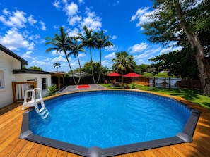 A swimming pool with a basketball court, palm trees, and a wooden deck.