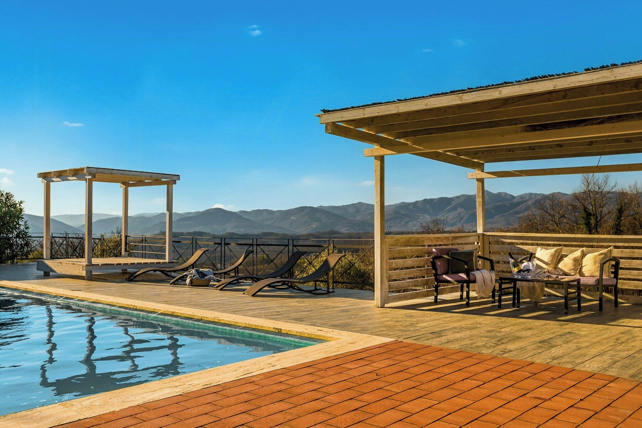 Área de piscina com espreguiçadeiras e um pergolado com vista para as montanhas.