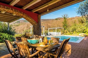 Une terrasse couverte avec une piscine, des meubles en bois et une vue sur le paysage environnant.