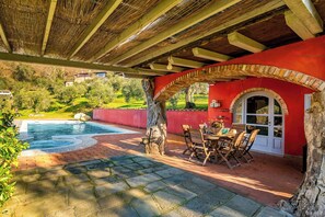 Un espace extérieur abrité doté d’une piscine, d’un sol en pierre, de mobilier en bois et d’un mur rouge agrémenté d’une fenêtre en arc de cercle.