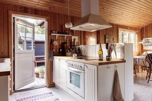 A kitchen with wooden walls, a central island, a stove, and a hanging light fixture. - Authentic summerhouse near the beach (Rørvig)