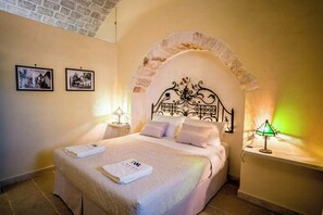 A neatly made bed with a headboard, two bedside tables with lamps, and two framed pictures on the wall. - Restored trullo with pool near Alberobello (Martina Franca)