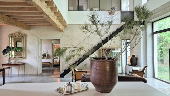 Ein geräumiger Raum mit einer großen Topfpflanze, einem Holztisch mit Tablett und einer Treppe, die zu einer oberen Ebene führt.