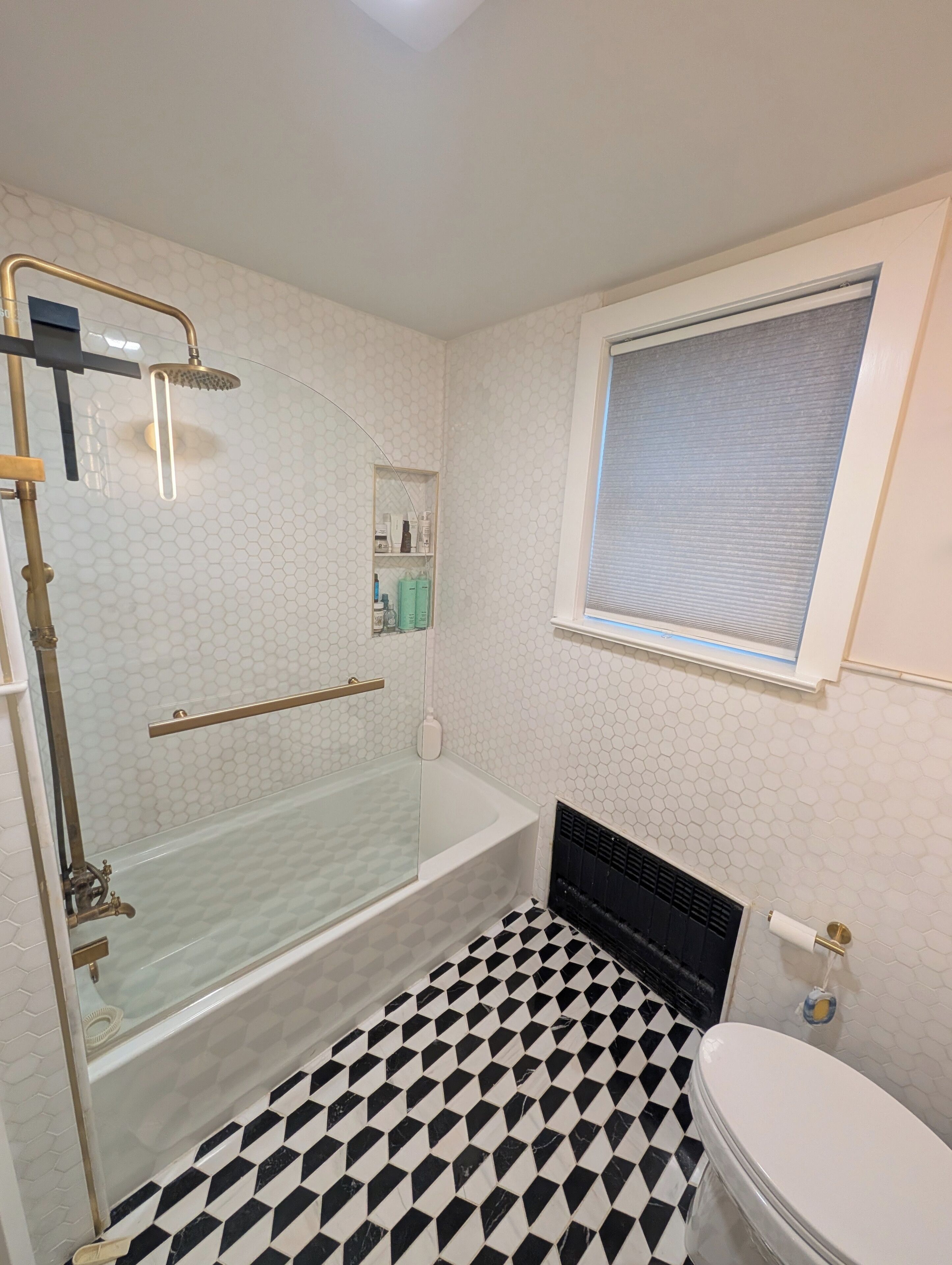 Une salle de bain avec une douche à parois de verre, une baignoire, des toilettes et une fenêtre avec des stores.