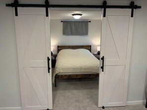A bedroom with a bed, two nightstands, a lamp, and a sliding barn door. - Spacious 4BR Home w/ Epic Basement Arcade (Rapid City)