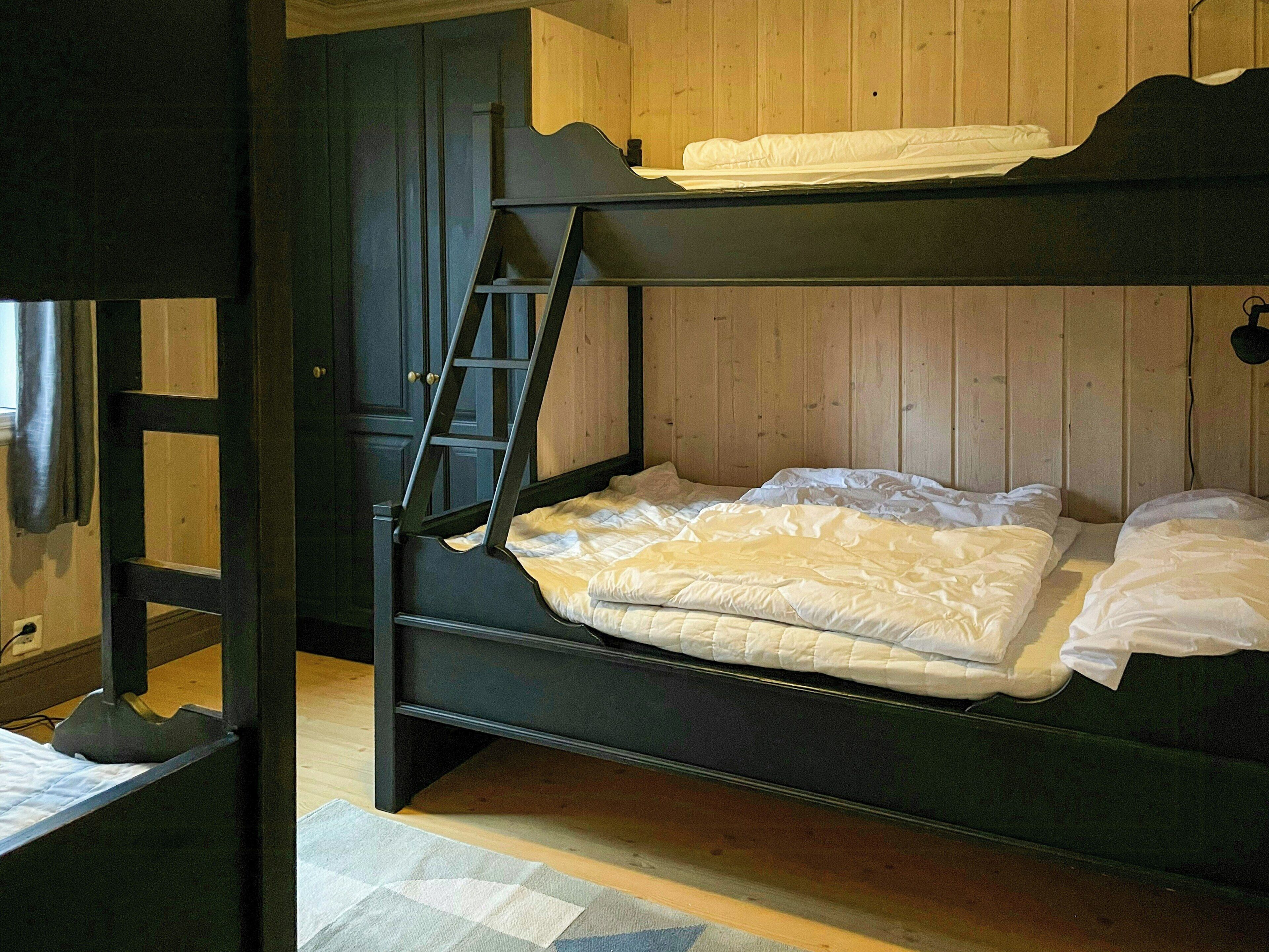 Un lit superposé avec une échelle, des murs en bois et une fenêtre avec des rideaux.