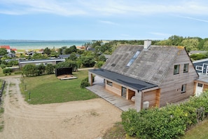 Ein modernes Haus mit Satteldach, einer Holzterrasse und Blick auf das Meer.