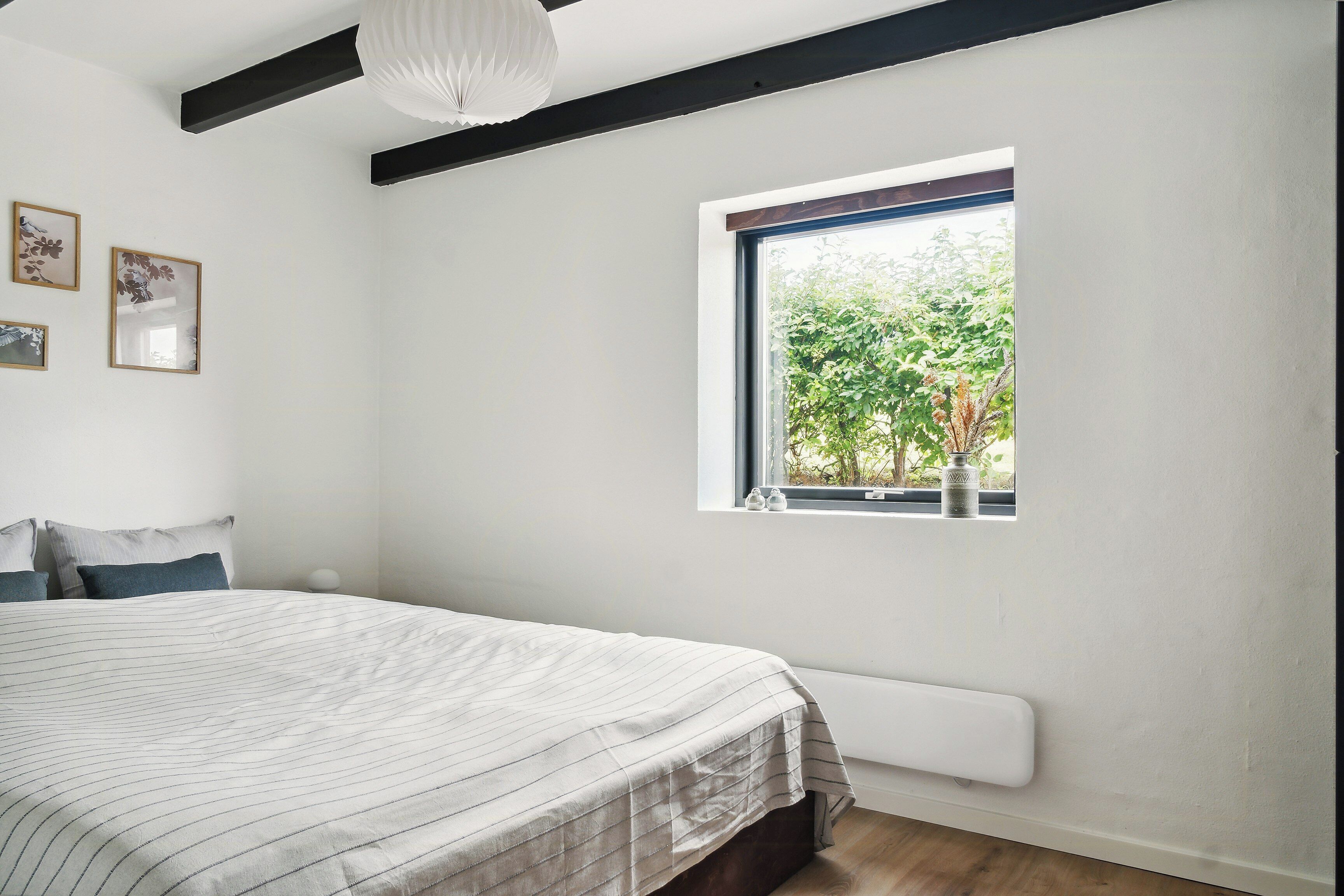 A bedroom with a bed, a window with a view of greenery, and a radiator.