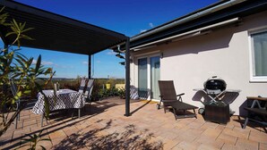 Een terras met buitenmeubilair, een barbecue en een overdekt gedeelte.