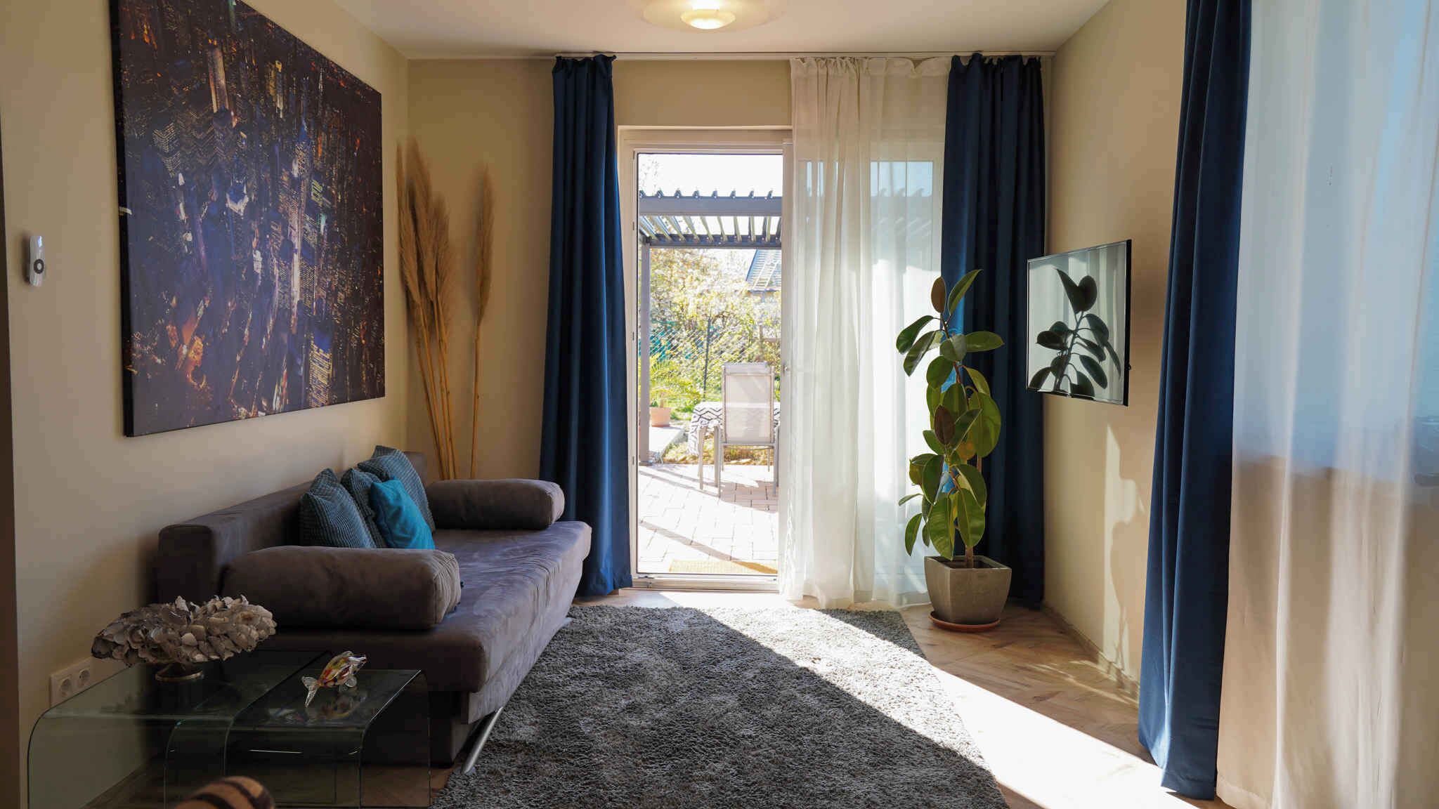 Een woonkamer met een bank, een salontafel, een groot abstract schilderij, een potplant en een uitzicht door een glazen deur op een terras.