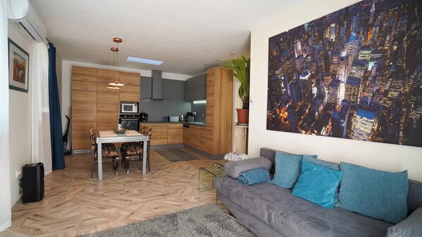 A modern living space with a dining area, kitchen, and a large cityscape painting.