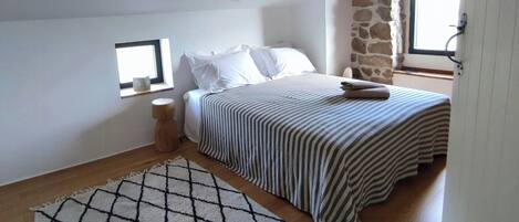 Een slaapkamer met een bed, een raam, een stenen muur en een houten balk.
