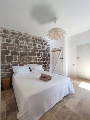 Ein Schlafzimmer mit Steinwand, einem Bett mit weißer Bettwäsche, einem hölzernen Nachttisch und einer Pendelleuchte.