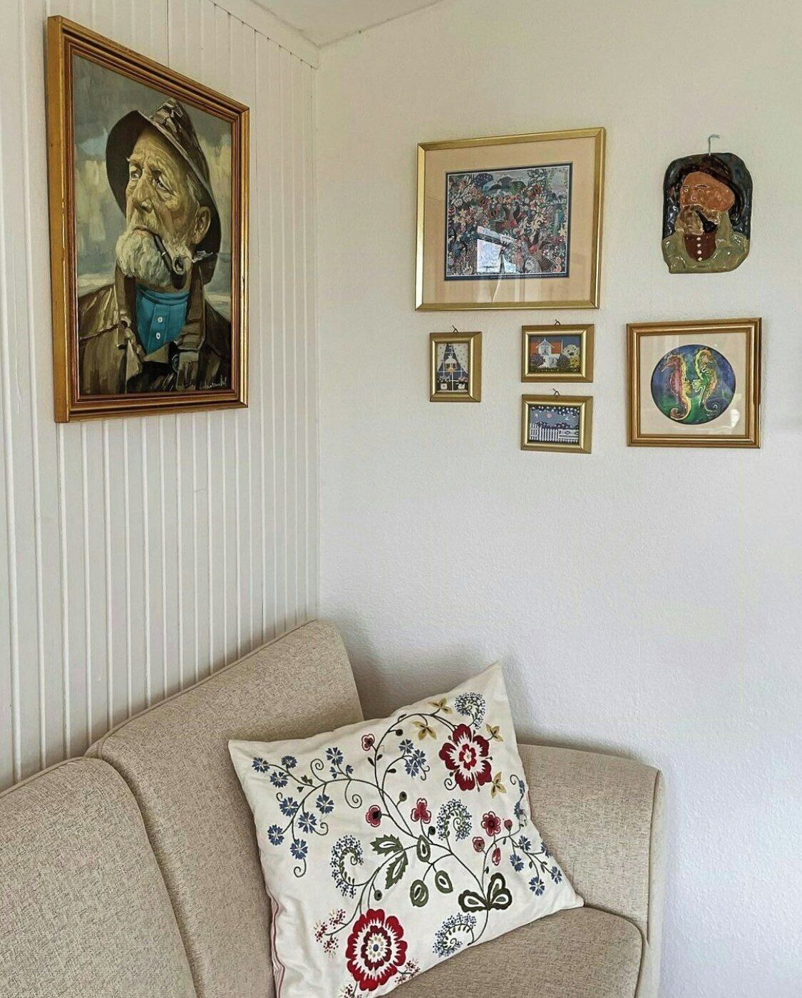 A living room with a beige sofa, a decorative pillow, and several framed artworks on the wall.
