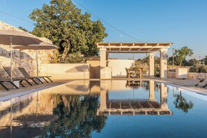 Ein Pool mit Pergola, Liegestühlen und einer Steinmauer.