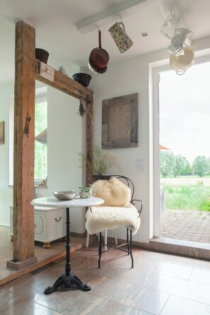 Ein Zimmer mit einem spiegelnden Holzbettrahmen, einem weißen Tisch mit einer Schale, einem flauschigen Sessel und Blick auf Grünflächen.