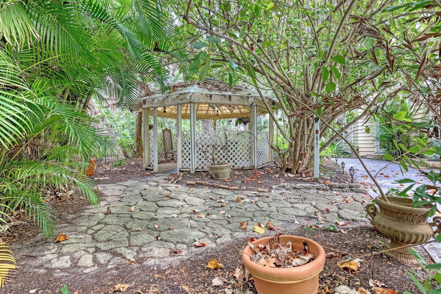Un jardín con pérgola, sendero de piedra y plantas en macetas.