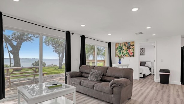A modern living room with a large window, a sofa, a glass coffee table, and a view of the outdoors. - Private 2bd Historic River Estate Walk EGAD Kayaks (Melbourne)