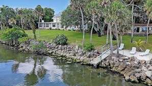 A waterfront property with a dock, lounge chairs, and a large house in the background. - Private 2bd Historic River Estate Walk EGAD Kayaks (Melbourne)