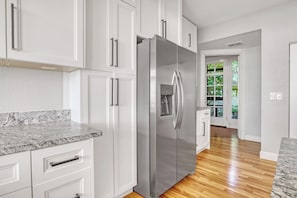 Eine Küche mit weißen Schränken, einem Edelstahlkühlschrank, Granit Arbeitsplatten und Holzböden.