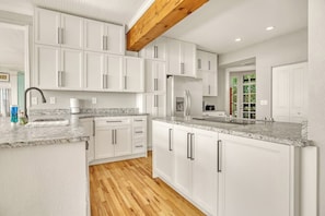 Eine moderne Küche mit weißen Schränken, Granit Arbeitsplatten und einem Holzbalken an der Decke.