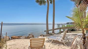 Une plage avec deux palmiers, une terrasse en bois et deux chaises longues.