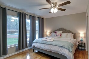 Ein Schlafzimmer mit Bett, Deckenventilator, Fenster mit Vorhängen und Blick auf einen Pool.