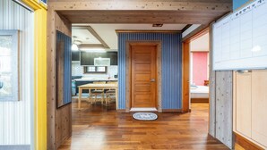 Un couloir doté d’un plancher en bois, d’une porte en bois et donnant sur un espace cuisine.